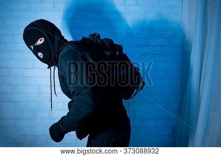 Marauding Concept. Stealthy Criminal Wearing Black Mask And Hooded Sweatshirt Sneaking In House At N