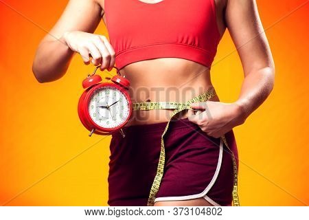 Woman In Sportswear Holding Alarm Clock And Meter. People, Fitness And Healthcare Concept