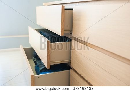 Open Chest Of Drawers Made Of Wood, Side View. Inside Are Things, Clothes, Jeans. Close-up.