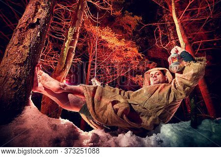 Medieval Monk In Canvas Sackcloth Robe With Lattern Resting On Snow In Dark Forest And Red Light On 