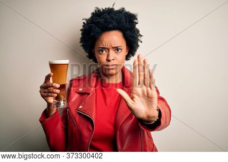 Young African American afro woman with curly hair drinking glass of beer with alcohol with open hand doing stop sign with serious and confident expression, defense gesture