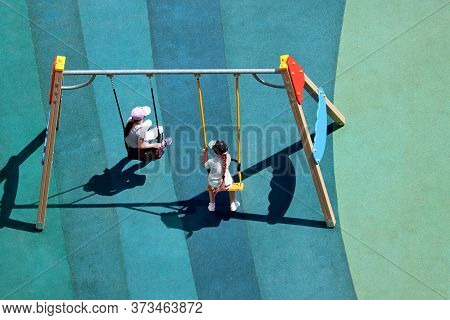 Children Swinging On The Playground Swings, Top View. Two Little Girl Playing Together, Leisure In S