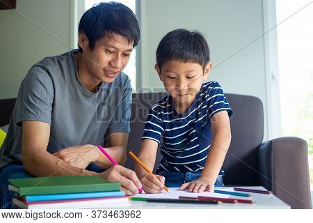 Family And Homework Concept. Happy Father And Son With Book Writing To Study At Home.