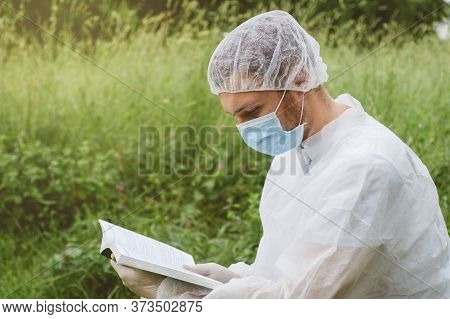 Man Reading A Book In Protective Clothes. Covid-19.