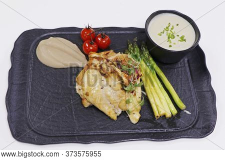 Corn Fed Chicken Breast With Potato Mash, Asparagus And Cherry Tomato In A Black Plate