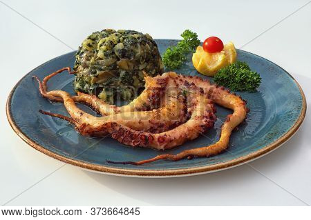 Balkan Cuisine. Plate With Grilled Octopus And Green Leafy Vegetables On White Table. Free Space For