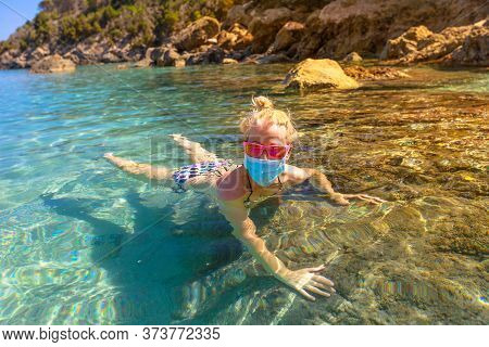 Woman Swimming In Fetovaia Beach And Crystal Sea With A Surgical Mask During Covid-19. Blonde Touris