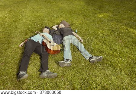 Two Men On City Park Summer Meadow Enjoying Day With Guitar