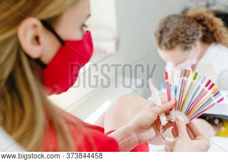 Woman wearing face mask checking colors for toenail pedicure while podiatrist is working