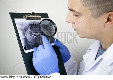 A Dentist Doctor Examines A Radiography Of The Teeth Of A Patient Who Has Problems And Teeth Are Ins