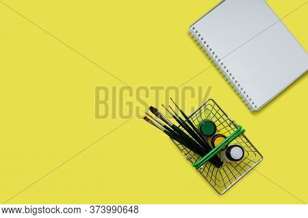 A Flat Layer Of Metal Shopping Basket With Artistic Colors: Yellow, Green And White, Brushes And A W