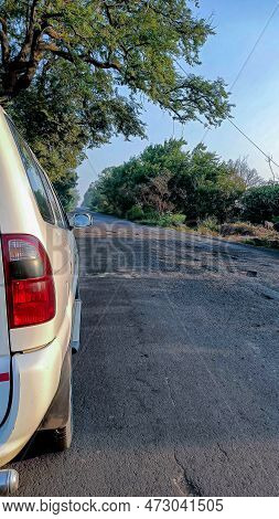 Stock Photo Of A White-colored Car Parked On The Side Of An Empty Asphalt Road Surrounded By Green T