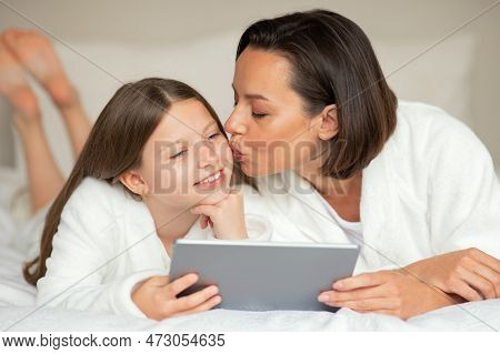 Smiling Young Lady Kiss On Cheek Little Caucasian Girl In Bathrobe, Watch Video On Tablet, Relaxing 