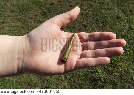 Rifle Cartridge In Hand On A Background Of Green Grass. Close-up