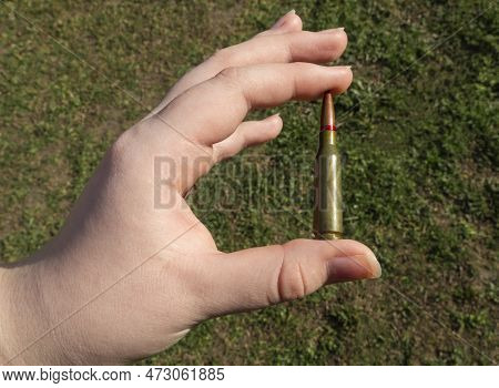 Rifle Cartridge In Hand On A Background Of Green Grass. Close-up