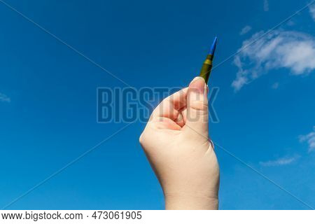 Yellow-blue Rifle Cartridge In Hand Against The Blue Sky (national Symbols Of Ukraine). The Concept 
