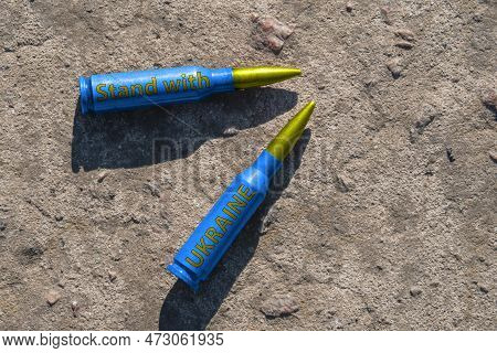 Two Yellow-blue Rifle Cartridges With The Inscription Stand With Ukraine Lie On A Concrete Surface (