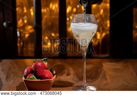 Glass Of Brut Champagne Bubbles Wine In Tulip Glass And Bowl With Fresh Strawberries On Evening Bar