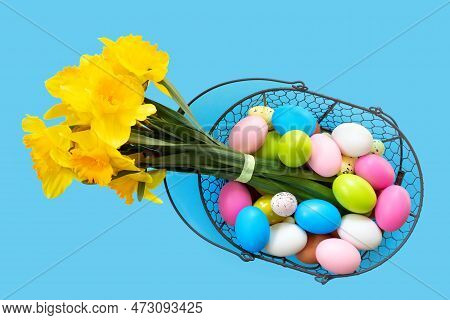 Basket With Easter Eggs And Bouquet Of Yellow Narcissus On Blue Paper Background. Flat Lay  Top View