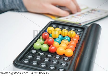 Close Up Board Game With Black Field And Colorful Balls In Holes Against Blurred Hand With Game Rule