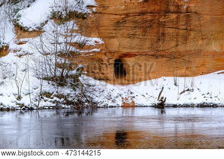 Red Sandstones On The Bank Of The River Salaca. Red Sandstone Rock In Bezdeligu Winter. Skanaiskalns
