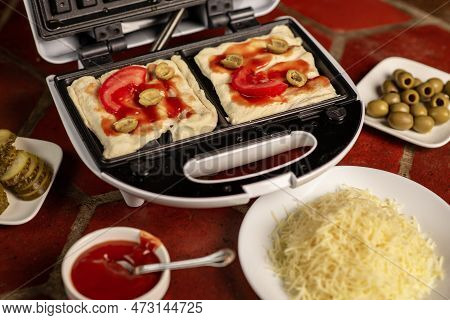 Cooking Pizza Waffle, Piffle. Waffle Iron And Different Ingredients On The Kitchen Table.