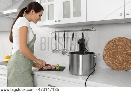 Woman Cutting Meat Near Pot With Sous Vide Cooker In Kitchen. Thermal Immersion Circulator