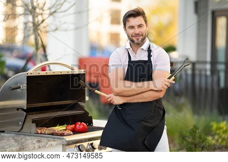 Barbecue Master. Middle Aged Hispanic Man In Apron For Barbecue. Roasting And Grilling Food. Man Hol