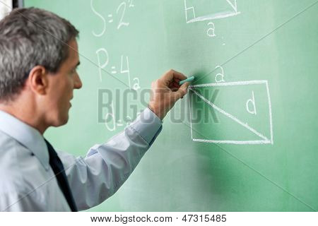 มุมมองด้านข้างของอาจารย์ชายผู้ใหญ่เขียนบน greenboard ในห้องเรียน