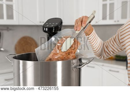 Woman Putting Vacuum Packed Meat Into Pot With Sous Vide Cooker In Kitchen, Closeup. Thermal Immersi
