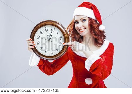 One Winsome Gleeful Red-haired Santa Helper With Big Round Clock And Showing Time Posing Against Whi