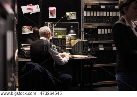 Senior Federal Agent Sitting At Desk Table In Arhive Room, Analyzing Crime Evidence Documents. Polic