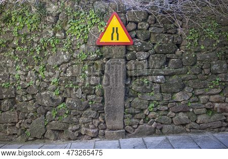 Narrowing Yellow Sign Attached To Old Stone Wall Of Rural Area. Driving At Villages Concept