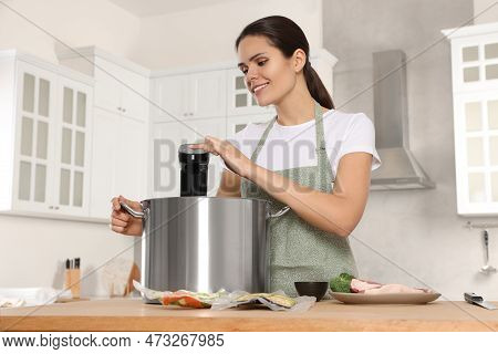 Woman Using Thermal Immersion Circulator At Table In Kitchen. Sous Vide Cooking