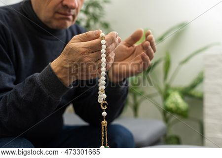 An Elderly Man Prays With A Rosary And The Flag Of The United Arab Emirates