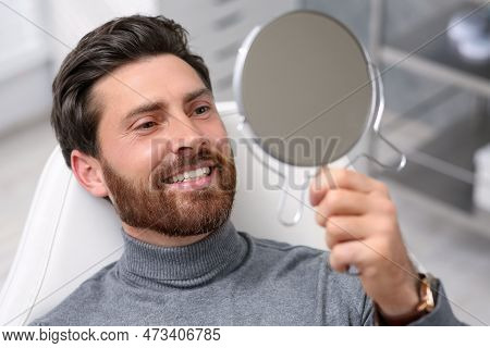 Man Looking At His New Dental Implants In Mirror Indoors