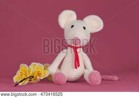 Amigurumi One White Mouse With Big Ears And Long Nose Sits On Pink Background Next To Yellow Orchid 