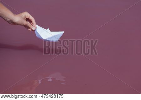 Female Hand Releases White Paper Boat To Float On The Surface Of Salty Pink Lake.