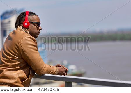 Depressed Young African Man Stands At The Top Of A Waterfront, Looking Down At The River. A Hapless 