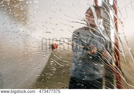 Man Washing Car With Water Gun In Carwash Self-service. Soap Sud, Wax And Water Drops Covering Vehic