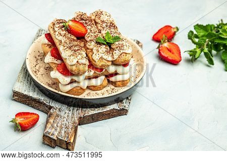 Italian Dessert Tiramisu Cake With Fresh Strawberry, Biscuit And Whipped Cream And Mint On A Light B