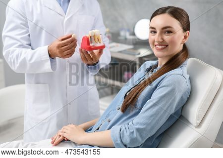 Doctor With Educational Model Of Dental Implant Consulting Patient In Clinic