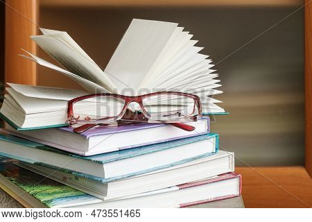 On The Wooden Surface Of The Table Lies A Stack Of Reading Literature With Women's Eyeglasses.