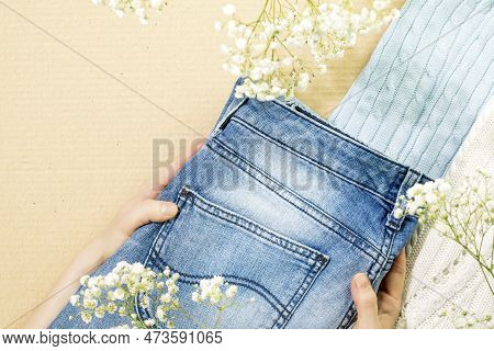 Female Hands Holding Jeans Near Sweaters On Cardboard Background