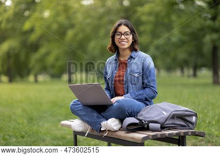 Smiling Arab Female Student In Eyeglasses Using Laptop Outdoors