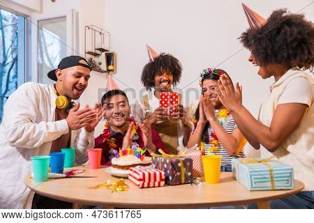 Multi-ethnic Group Of Friends At A Birthday Party On The Sofa At Home With A Cake And Gifts, Smiling