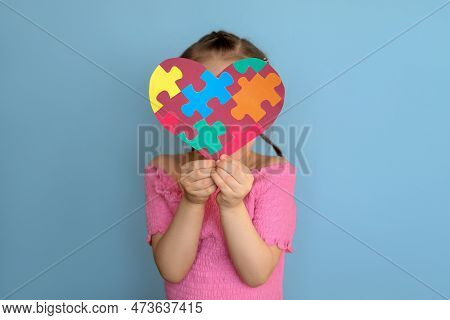 A Shy Timid Girl In A Pink T-shirt Covers Her Face With A Heart Made Of Colorful Puzzles. To Tell , 