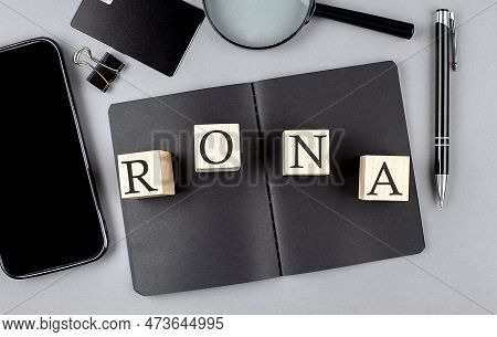 Word Rona On A Wooden Block On A Black Notebook With Smartpone, Credit Card And Magnifier