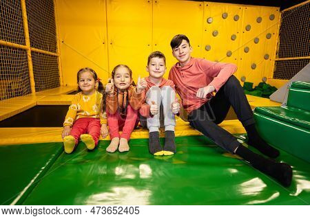 Four Kids Together Sit At Playground Park. Sisters And Brothers In Active Entertaiments.