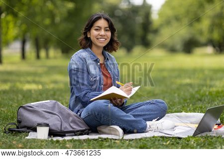 Middle Eastern Female Student Writing In Notepad While Preparing For Exam Outdoors